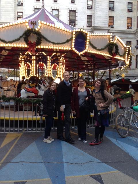 Ms. Liz, Mr. Chris, Ms. Liz, and Ms. Kate in front of carousel in City Hall courtyard.